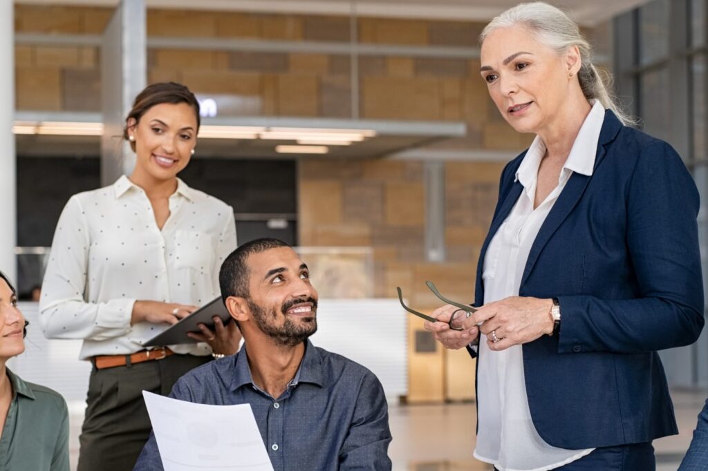 A manager speaks with her team while a colleague with a tablet and a seated team member listen