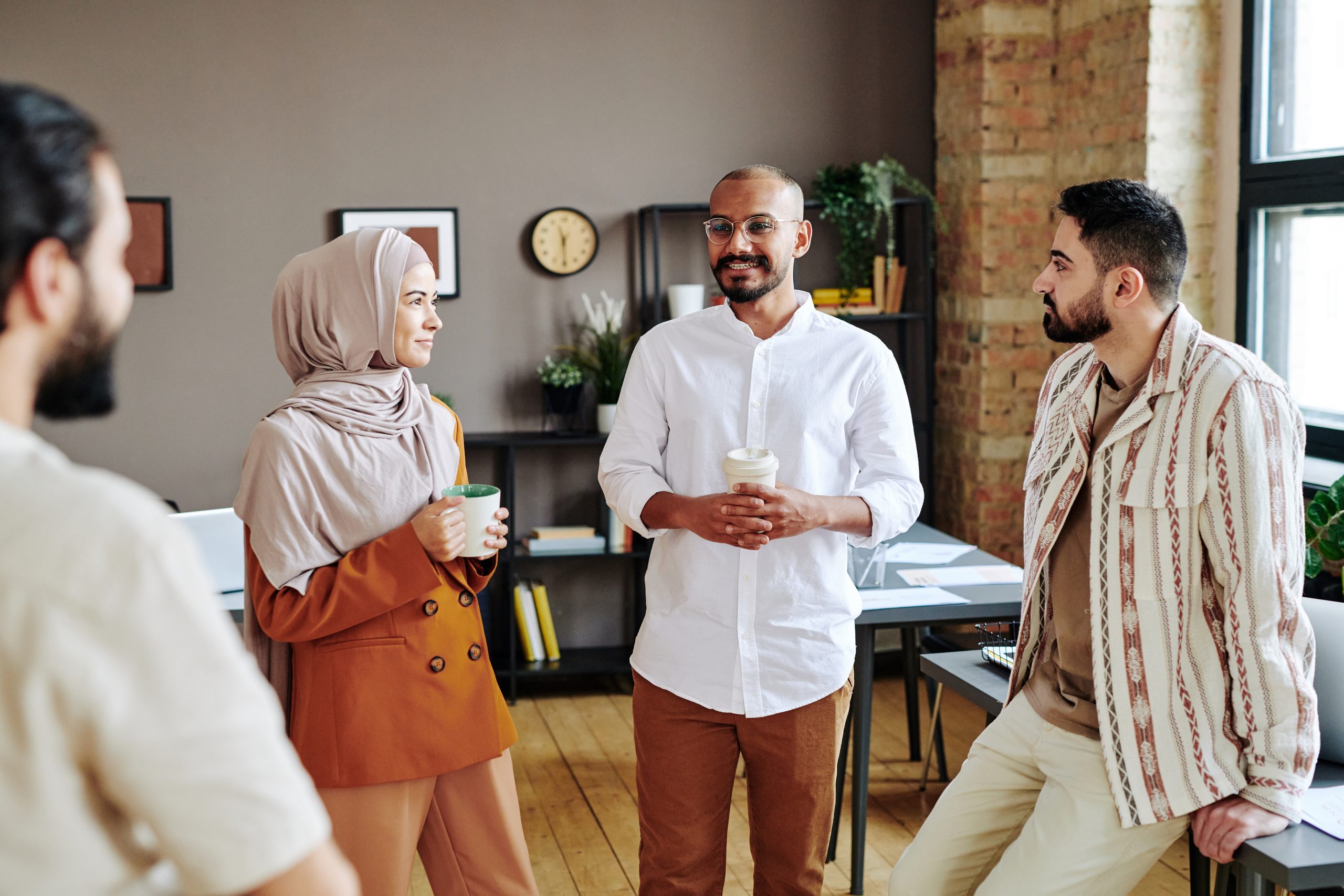 Four colleagues talk together in an open office, coffee cups in hand