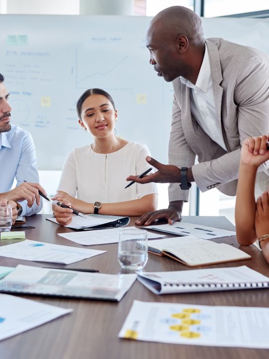 Business team engaged in a meeting, discussing strategies and reviewing documents at a conference table with charts and notes, in a modern office setting.